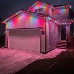 Two-storey home illuminated with colorful permanent outdoor LED lighting installed along the roofline.