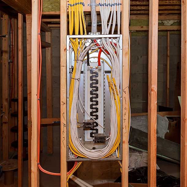 Electrical panel installation in progress within exposed wooden framing, showcasing organized wiring with yellow and white cables neatly arranged and secured for a residential setup.